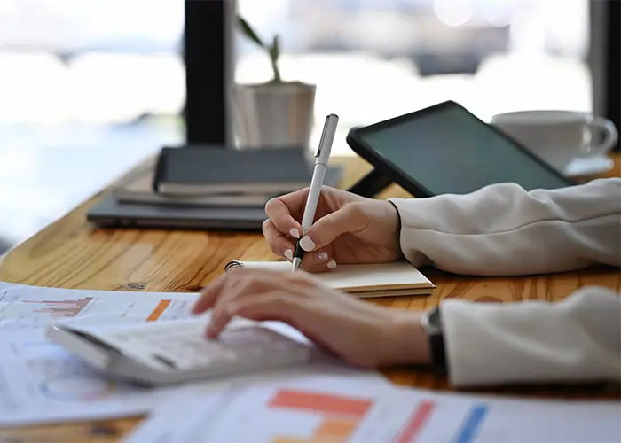 Persona trabajando en informes financieros con una calculadora y una tableta en un escritorio - LaoN Asesores